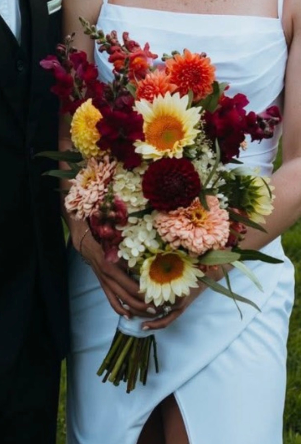 Bride holding a seasonal bouquet of cream sunflowers, peach dahlias, and burgundy blooms